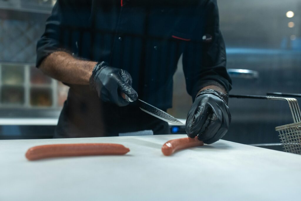 Chef slicing hot dogs before cooking them on the stove.