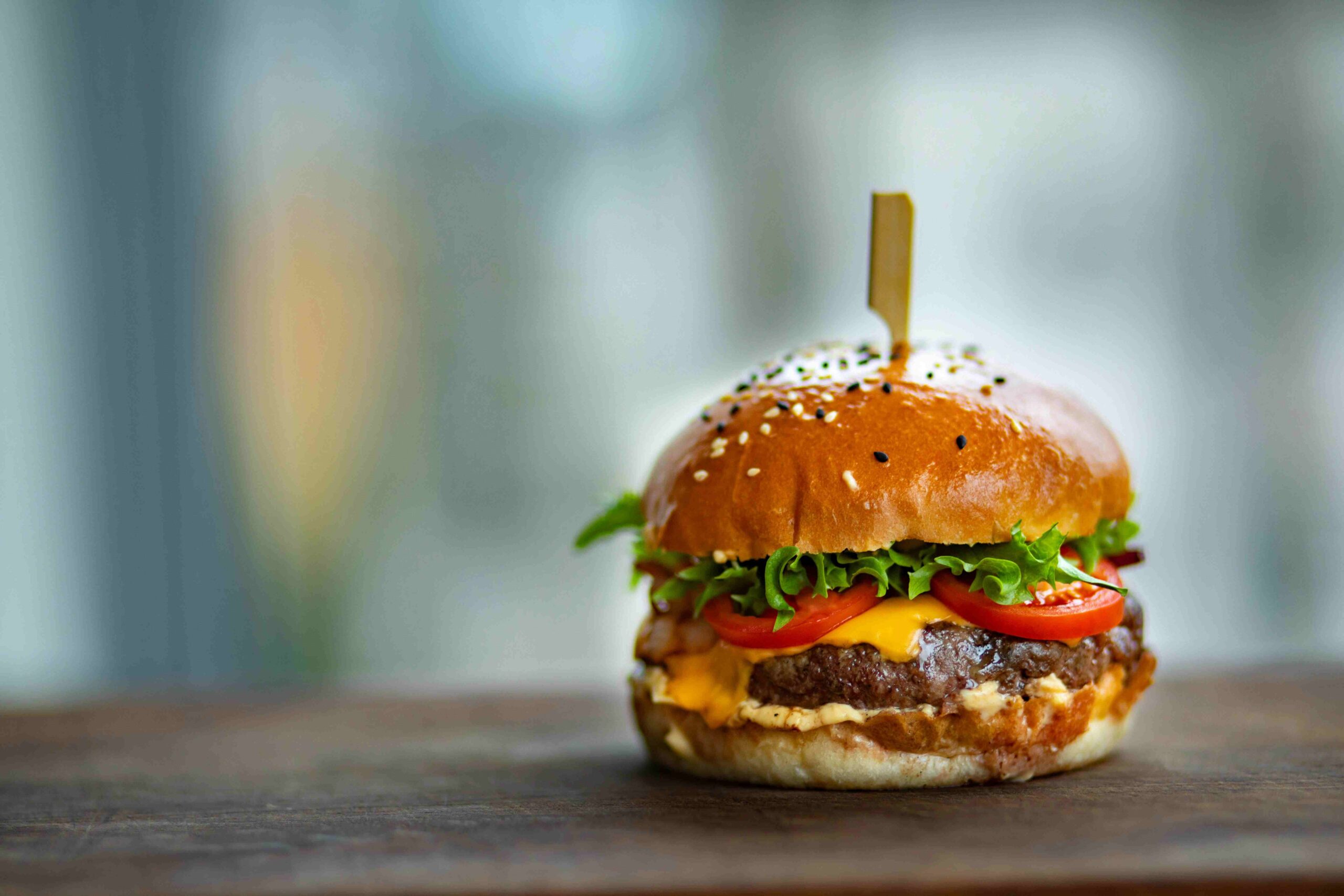 Fresh ingredients for homemade burgers, including ground beef, hamburger buns, cheese slices, lettuce, and tomatoes arranged on a kitchen counter.